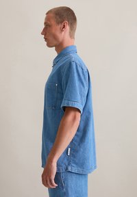 Lichtblauw denim shirt, korte mouwen, kraag, enkele borstzak, subtiele stiksels, normale pasvorm, label aan de zijnaad.