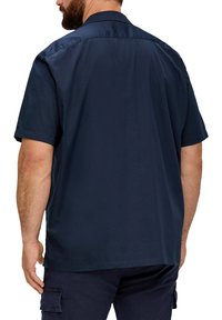 Kurzes navy Hemd aus glattem Stoff, mit klassischem Kragen, Rückenpasse und lässigem Schnitt. Dezente Nähte sind sichtbar.