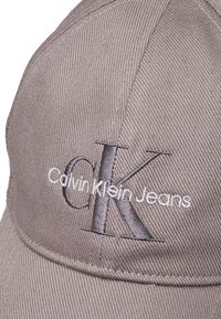 Hall hallide suvine müts, millel on valgest ja hallist tähistatud tikitud logo "Calvin Klein Jeans", struktureeritud kuju ja tekstureeritud kangas.