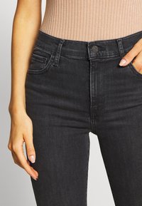 Jeans de mezclilla negros con un corte ajustado, que presentan bolsillos frontales y un cierre de botón visible en la cinturilla. Textura suave y costuras sutiles.