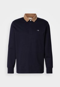 Polo a maniche lunghe blu navy con colletto in velluto a coste marrone, dotato di una patta con due bottoni e di un piccolo logo sul lato sinistro del petto.