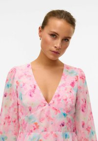 Blommig klänning i rosa chiffong med en djup V-ringning; har puffade långa ärmar och en flödande silhuett med livfulla blommönster.