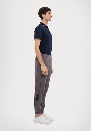 Polo shirt blu marine e pantaloni sportivi grigi con un accento a righe. I pantaloni sportivi presentano una vestibilità affusolata e un elastico in vita, abbinati a scarpe da ginnastica bianche.