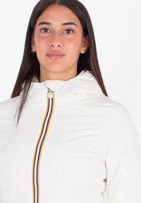 Witte hooded jas met ritssluiting aan de voorkant, voorzien van een meerkleurige streep. Glad textuur met subtiele branding op de borst en een getailleerd ontwerp.