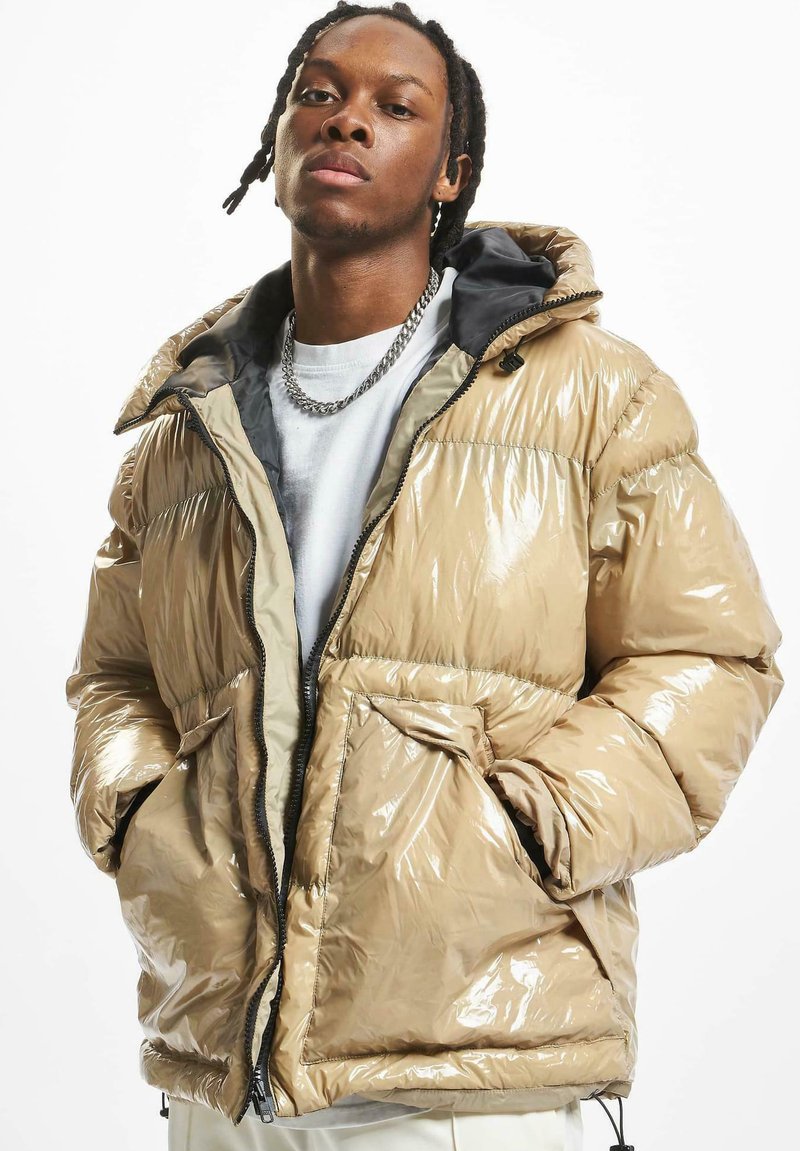Chaqueta puffer brillante en color beige con capucha, que presenta una textura suave, puños elásticos, cierre frontal con cremallera y dos bolsillos laterales.