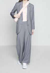 Gray pinstriped suit with loose trousers, single-breasted blazer, and a pink tank top. White sneakers and a soft pink shoulder bag.