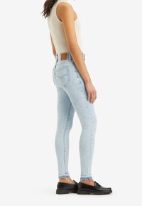 Jeans skinny azzurri chiari con vita alta, orlo sfrangiato e tasche, abbinati a una canotta beige a coste e mocassini neri.