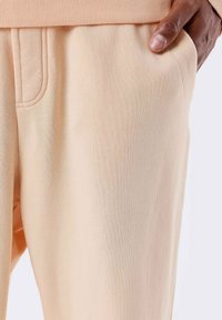 Pantalones de chándal en melocotón claro, hechos de una tela suave, con una cinturilla acanalada, bolsillos laterales y un detalle de costura minimalista.