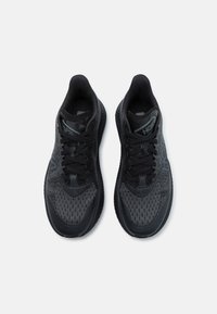Baskets noires de sport avec un dessus en tricot texturé, dotées d'une semelle en caoutchouc lisse et de lacets plats, affichant un design minimaliste avec un branding subtil.