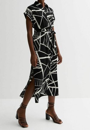 Black and white geometric patterned midi dress with short sleeves, side slit, waist tie, and strappy black block heel sandals.