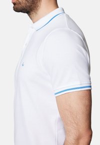 Biała koszulka polo z kołnierzykiem i mankietami w odcieniu niebieskim, wykonana z fakturowanej tkaniny z małym haftowanym logo na piersi.