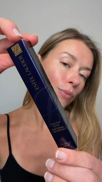 Estee Lauder Glossy Pout Lip Oil in een donkerblauwe doos met gouden accenten, met productdetails in witte tekst, vastgehouden door een persoon.
