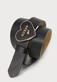 Ceinture en cuir noir avec une boucle en métal doré en forme de cœur portant la mention "GUESS girl" en relief. Texture lisse, longueur ajustable et extrémité effilée.