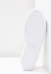 Biała podeszwa sneakerów z teksturowanym, diamentowym wzorem, z jasnopomarańczowym akcentem po boku i metką z logo blisko pięty.