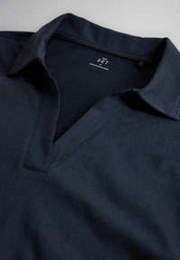 Dark navy blue polo shirt with a soft collar and deep V-neck, made in Bangladesh, shown flat on a light surface.