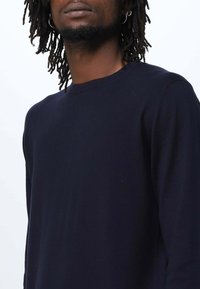 Maglione a maniche lunghe blu navy con collo rotondo, realizzato in un tessuto morbido, caratterizzato da una silhouette aderente e un design minimalista.