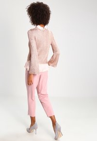 Světle růžový pletený svetr s rozšířenými rukávy, vrstvený přes bílou blůzu, doplněný o světle růžové kalhoty a šedé lodičky na vysokém podpatku.