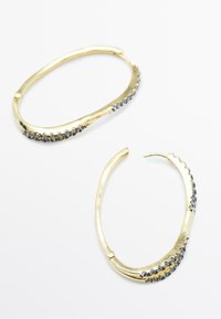 Orecchini a cerchio in oro con forma ovale, decorati con piccoli gemme scure lungo il bordo esterno, esposti su uno sfondo bianco.