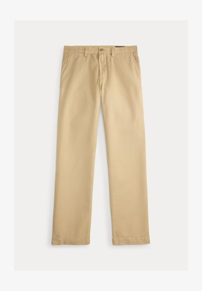 Beżowe spodnie o prostych nogawkach z szlufkami na pasek, z przodu zapięcie na guziki, zamek błyskawiczny i boczne kieszenie na jednolitym białym tle.