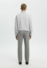 Pantaloni in lana grigi con vestibilità dritta e tasche posteriori, abbinati a una camicia button-up a righe leggere con bottoni ai polsini.