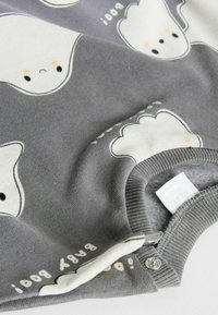 Bodysuit pour bébé gris avec des motifs de fantômes blancs et des accents de blush orange. Matière en coton doux avec des fermetures à pression et des poignets côtelés.