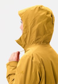 Giacca gialla impermeabile con cappuccio aderente, chiusura con zip e cordino regolabile. Texture liscia e design minimalista.
