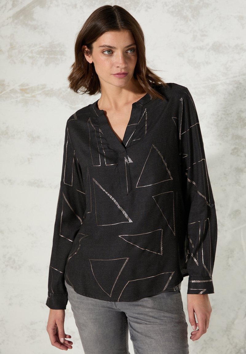 Chemise noire à manches longues avec un col en V, ornée de motifs géométriques métalliques et d'une coupe décontractée. Tissu doux avec des accents de couture visibles.
