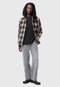 Camicia di flanella a quadri marrone e crema, abbinata a una maglietta nera e jeans larghi grigi. Scarpe nere completano il look.