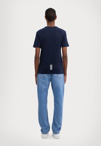 Marinblå bomull t-shirt med kort ärm, rund hals, med ett vitt randigt detalj på nedre delen av ryggen, parat med ljusblå denimjeans.