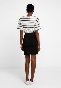 Falda negra con cinturilla elástica combinada con una camiseta blanca a rayas, de mangas cortas. El modelo lleva zapatillas blancas.