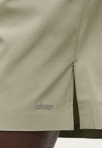 Πουκάμισο ελιάς κατασκευασμένο από απαλό ύφασμα με πλαϊνή σχισμή, διαθέτει γκρι λογότυπο "obey" στο τελείωμα. Ομαλή υφή και απλός σχεδιασμός.