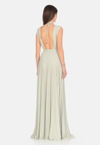 Abito lungo verde chiaro con texture plissettata, profondo scollo sulla schiena e nodo al collo a halter. Presenta una vita aderente e una gonna fluida.