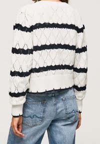 Woman wearing a white knitted sweater with black horizontal stripes and blue jeans, shown from the back.