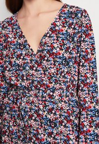 Blommig klänning i mörkblått med rosa, röd och grön mönstring. Har V-ringning, långa ärmar och ett midjeband för en åtsittande silhuett.