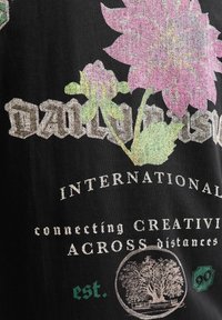 Sort stof med et livligt blomstermønster i pink og grøn. Teksten lyder "DAILY," "INTERNATIONAL," og "connecting CREATIVITY." Bemærkelsesværdige detaljer inkluderer et cirkulært grafisk element af et træ.