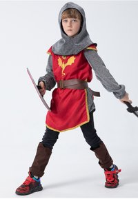 Child wearing a red knight costume with a dragon emblem, gray chainmail sleeves, brown belt, and black pants. Holding a shield and sword.