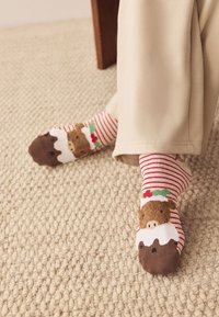 Baumwollsocken mit rot-weißen Streifen, versehen mit einem Bären, der einen Weihnachtshut trägt, und einem schokoladenmusterbesetzten Bündchen. Strukturierte Strickoptik.