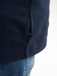 Tmavě modré tričko s krátkým rukávem, vyrobené z texturované látky, s bočním rozparkem a malou visačkou na lemu. Švy jsou úhledné a čisté.