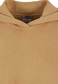 Sweat à capuche en coton beige avec couture double, affichant l'étiquette de la marque "Urban Classics" et la taille XS, fabriqué au Pakistan.