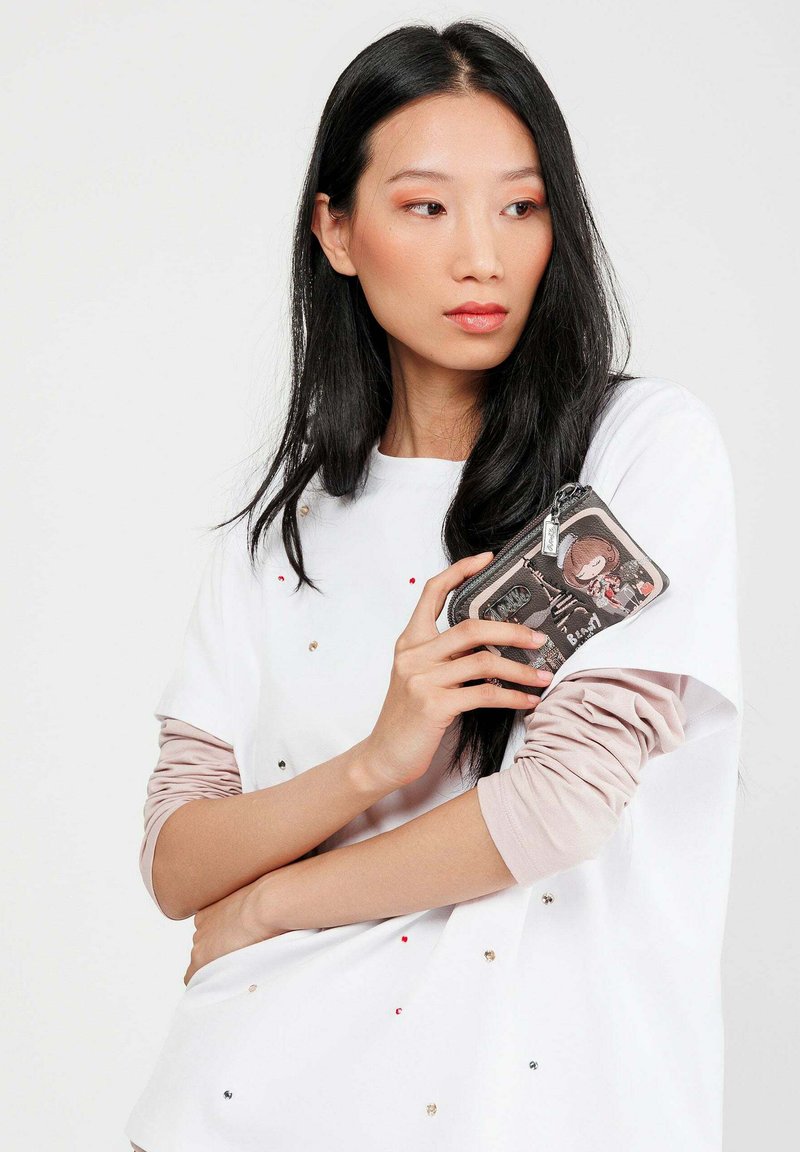 Camicia bianca a maniche corte con decorazioni multicolori, abbinata a un sottogiacca a maniche lunghe di colore rosa chiaro. Tieniti tra le mani una borsa a pochette con zip decorata con un motivo a cartoni animati.
