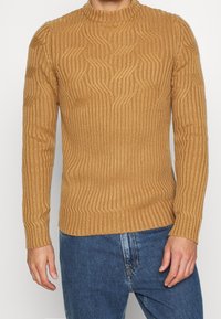 Pull ajusté à manches longues en maille nervurée texturée, couleur camel, avec encolure ronde et ourlet droit. Design décontracté.