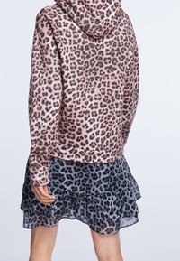 Mikina s leopardím potiskem v růžové a černé barvě, s přední kapsou a jemnou texturou. V kombinaci se sukní se sklady v černé a šedé barvě s leopardím potiskem.