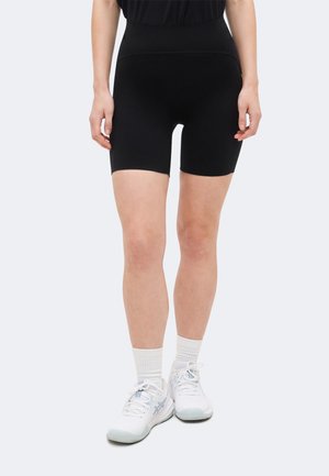 Άτομο που φοράει μαύρα εφαρμοστά σορτς, άσπρες κάλτσες και άσπρα αθλητικά παπούτσια, στέκεται με τα χέρια χαλαρά δίπλα στο σώμα.