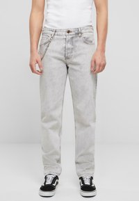 Heledad hallhall jeans sirge lõikega, viie tasku ja kettdetailiga ees. Kombineeritud mustade tennistega.