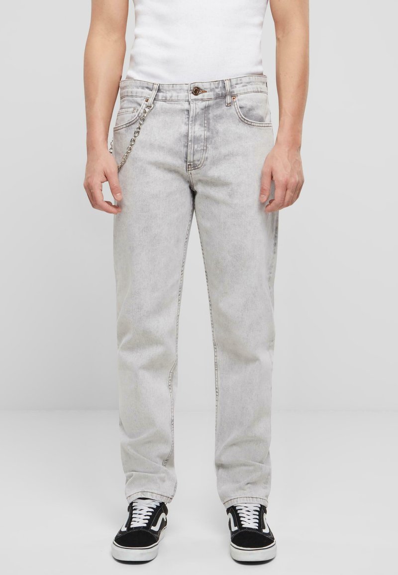 Heledad hallhall jeans sirge lõikega, viie tasku ja kettdetailiga ees. Kombineeritud mustade tennistega.
