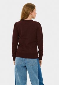 Bordo pulover s nabranim rukavima, rebrastim izrezom i manžetama, u kombinaciji s svijetloplavim wide-leg trapericama; glatka tekstura tkanine.