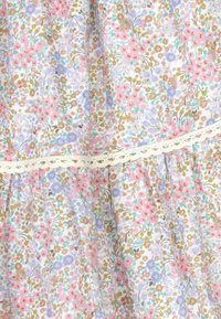 Tejido floral en tonos pastel de rosa, azul y verde con un fondo blanco. Presenta un borde de encaje y pliegues recogidos para aportar textura.