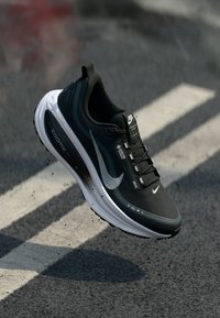 Zwart-witte Nike hardloopschoen met zichtbare Air Zoom zool, Gore-Tex label, zwevend boven een asfaltweg met witte belijning.