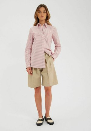 Chemise à rayures roses à boutons, avec une coupe droite, associée à un short beige plissé. Des chaussures noires avec une semelle blanche et des sangles complètent l'ensemble.
