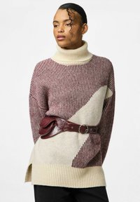 Pletený svetr s vysokým rolákem, sepraný pruhy v barvě kaštanově červené a smetanové. V kombinaci s širokým hnědým páskem, který dodává strukturovaný akcent. Černé kalhoty.